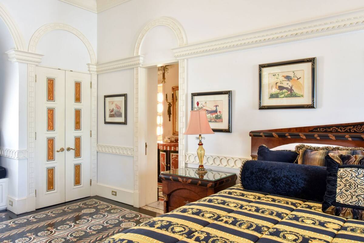 Una habitación con una cama, una mesita de noche, una lámpara, un cuadro enmarco y una puerta con paneles decorativos.