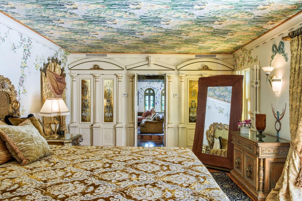 Una habitación con cama, espejo, cómoda y puerta que da a otra estancia.