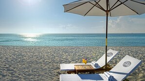 A beach with two sun loungers under a large umbrella, a wooden table, and a clear view of the ocean. - The Villa Casa Casuarina (Miami Beach)