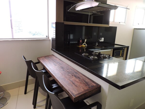 A compact kitchen with a central island, a gas stove, and a microwave. - Flat Residencial - La Residence (Goiania)