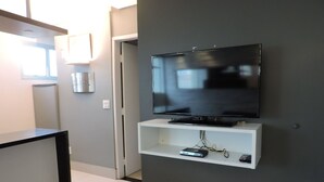 Uma sala de estar moderna com uma TV de tela plana presa a uma parede cinza, um móvel branco embaixo e uma mesa de centro preta à esquerda.