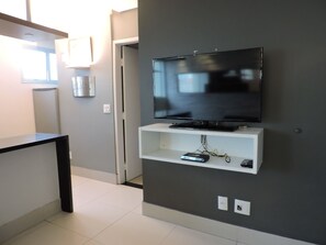 Ein modernes Wohnzimmer mit einem flachbildfernseher an einer grauen Wand, einer weißen Unterhaltungseinheit darunter und einem schwarzen Couchtisch links.