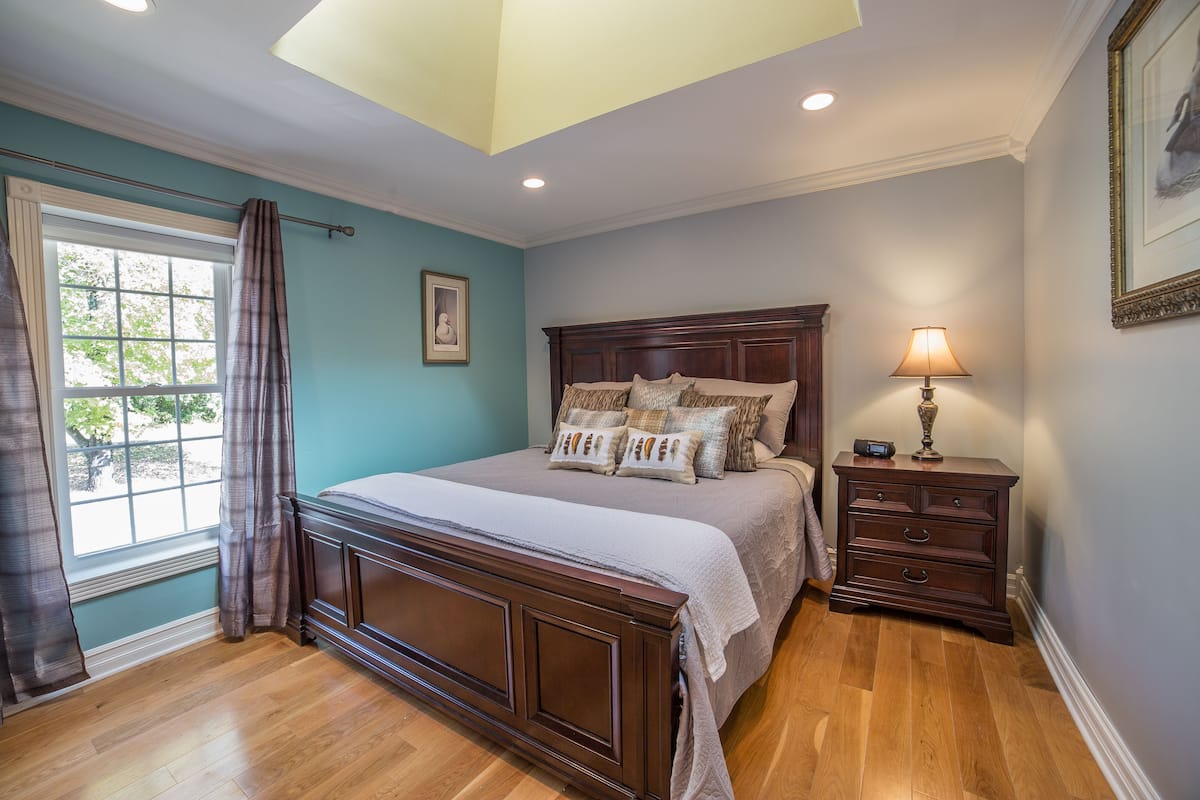 Un dormitorio con una cama grande, una mesita de noche con lámpara y una ventana con cortinas.