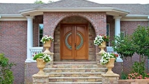 A brick house with a double wooden door, stone steps, and two flower pots on either side.