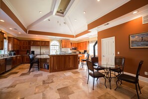 Una cocina amplia con armarios de madera, una isla central y un comedor con sillas y una mesa de vidrio.