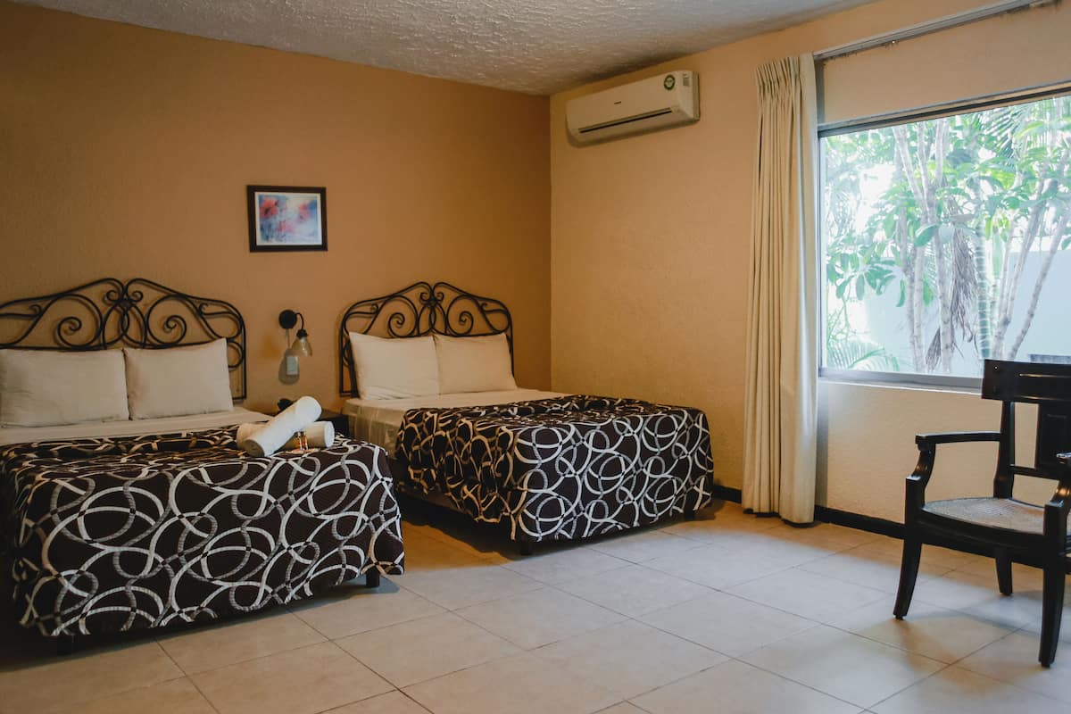 A room with two beds, a chair, an air conditioner, a window with curtains, and a framed picture on the wall.