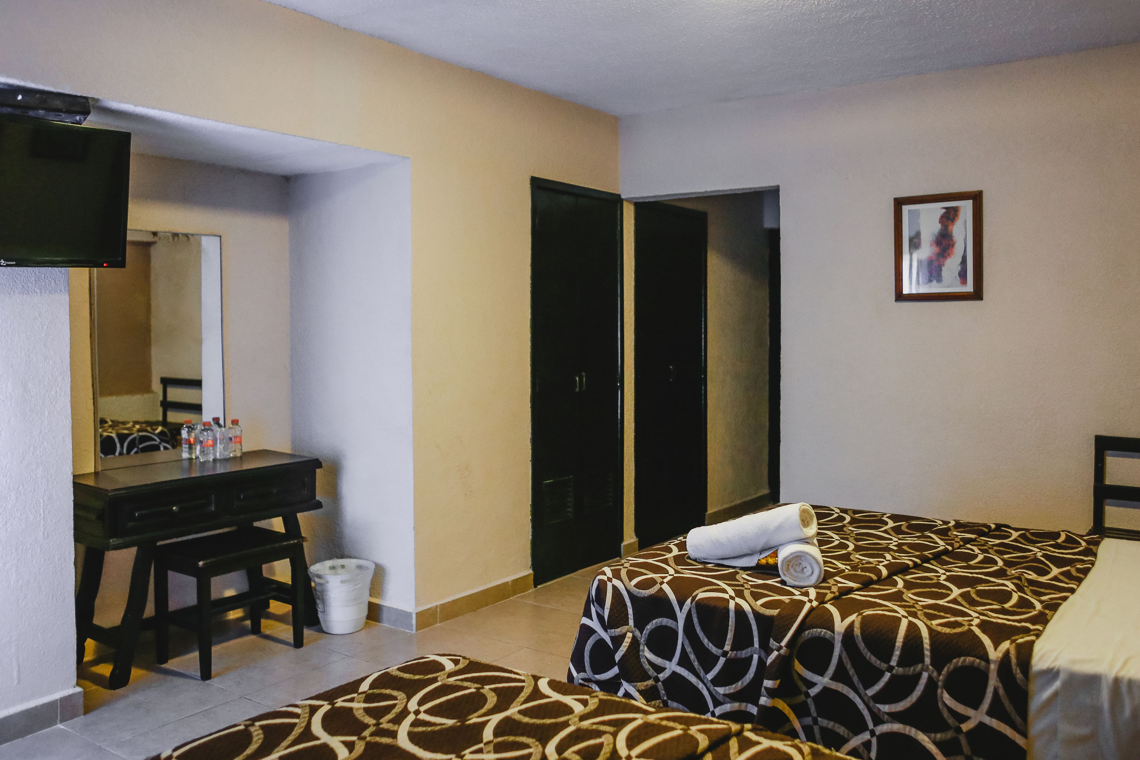Een hotelkamer met een bed, een bureau, een stoel, een spiegel, een schilderij aan de muur en een prullenbak.