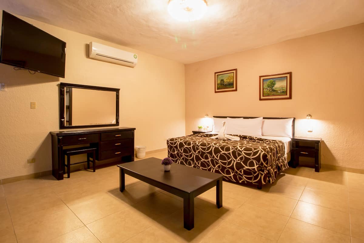 A bedroom with a bed, bedside tables, a desk, a chair, a TV, and an air conditioner.