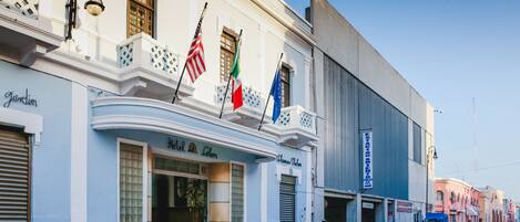 A building with a white facade, a balcony with lattice railings, and flags including the American and Italian flags.