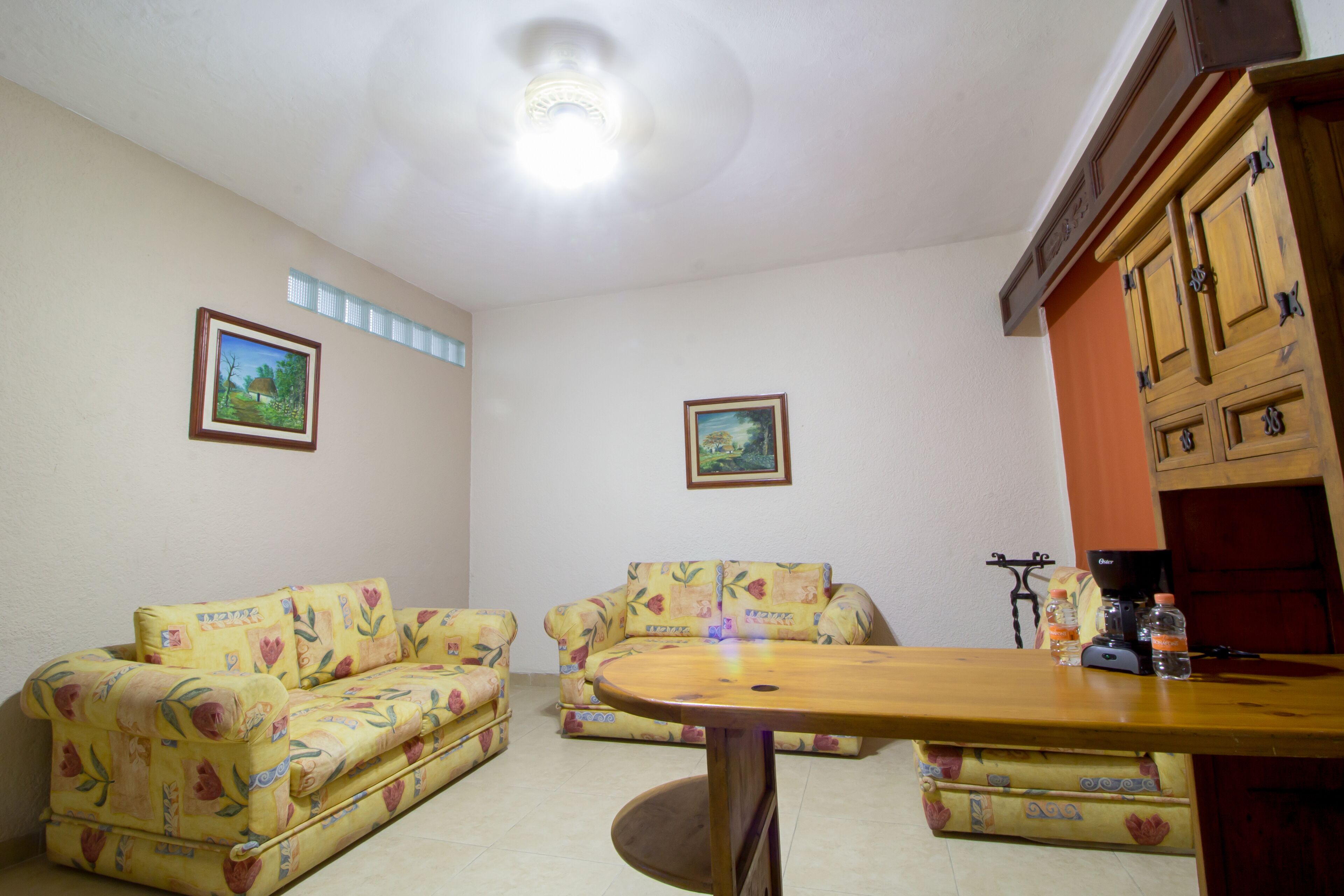 A living room with two floral-patterned sofas, a wooden coffee table, and a cabinet with bottles and a coffee machine.