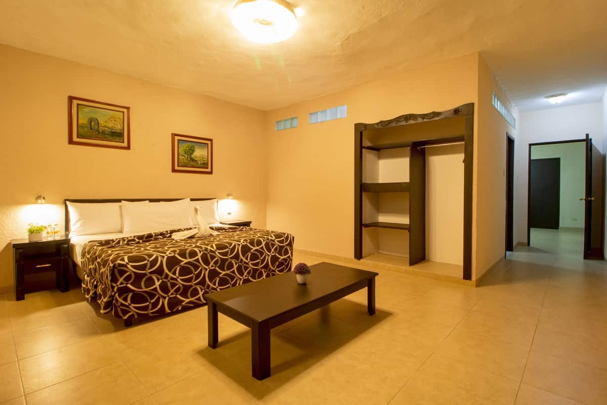 A hotel room with a bed, bedside tables, a small table, a wardrobe, and a door leading to another room.
