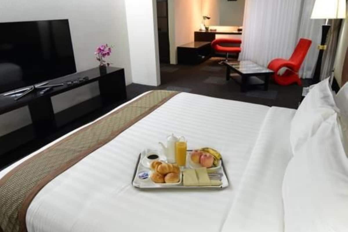 A hotel room with a bed, a TV, a desk, and a tray of breakfast items.