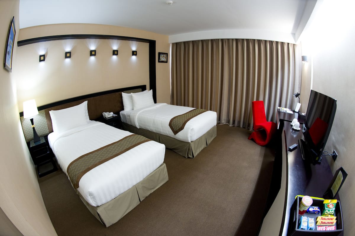A hotel room with two beds, a desk with a computer, a TV, and a minibar.