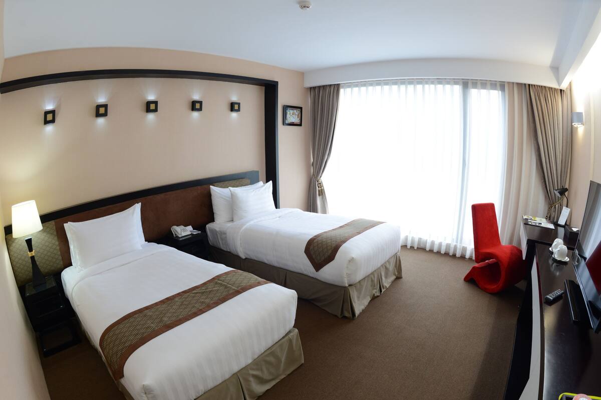 A hotel room with two beds, a desk, a TV, and a red chair.