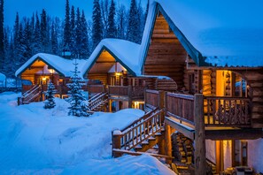 Une cabane en rondins avec une terrasse en bois et un escalier menant à l’entrée.