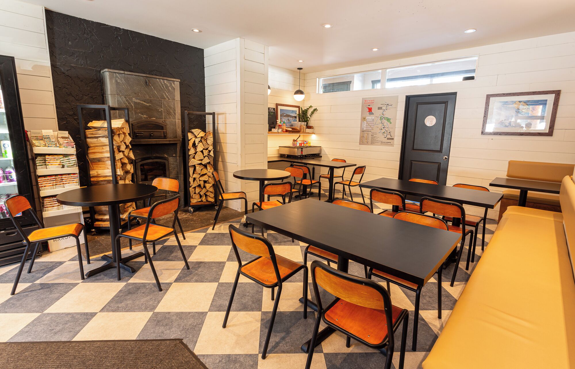 A cozy cafe with checkered flooring, wooden furniture, a fireplace, and a variety of seating options.