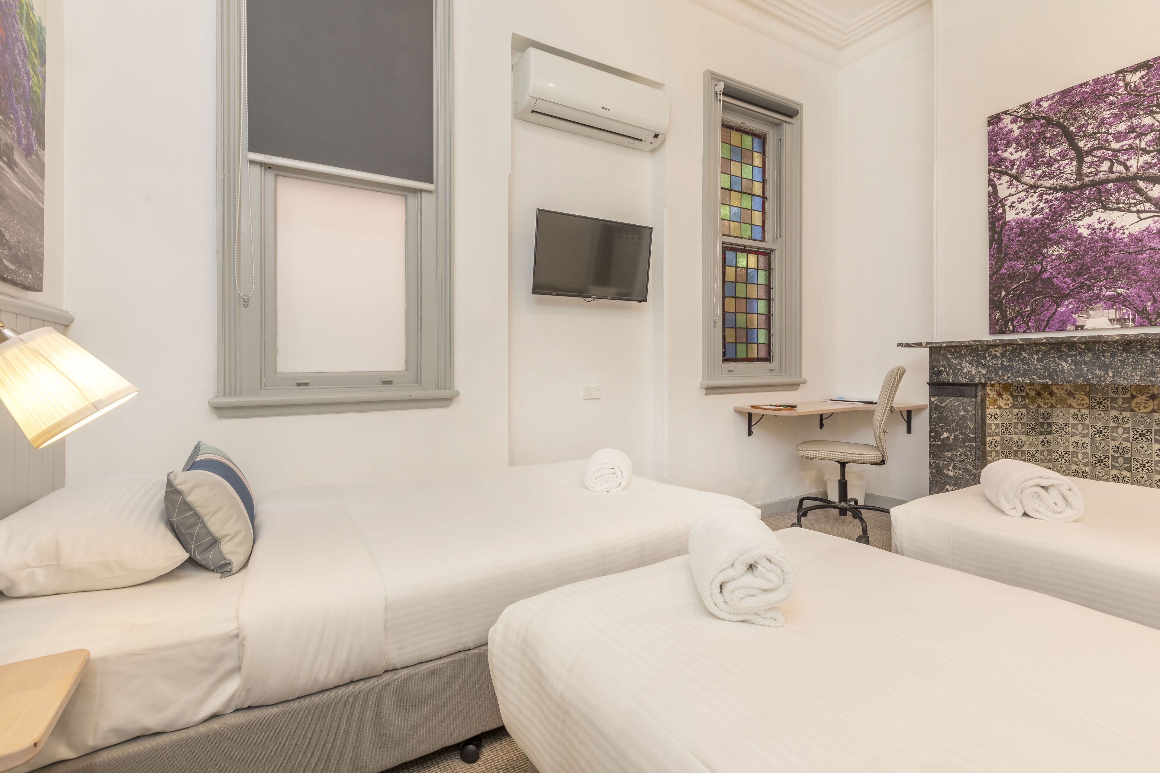 Ein Hotelzimmer mit zwei Betten, einem Schreibtisch, einem Sessel, einer Klimaanlage, einem Fernseher und einem Kamin.