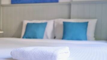 A neatly made bed with white bedding and blue pillows, a white towel on the bed, and a painting on the wall in the background.