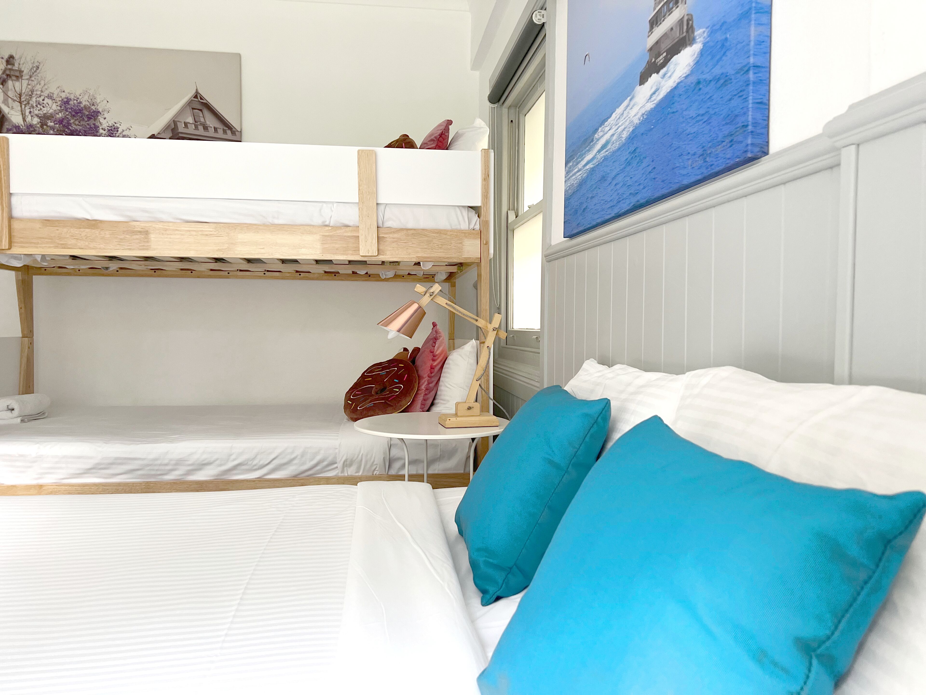 Una camera con letto a castello, una scrivania, una lampada e un quadro raffigurante un faro.
