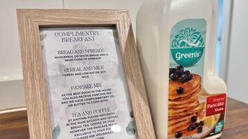 Un menú enmarcado que muestra opciones de desayuno y un envase de batido de panqueques Green's Original.