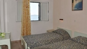 Un dormitorio con cama, una ventana con cortinas, una mesita con un florero y un cartel en la pared.