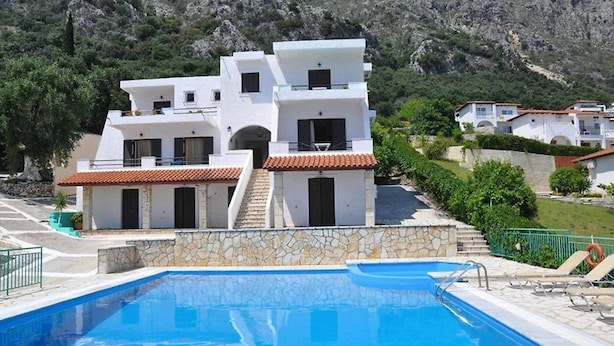 Un edificio moderno con piscina, muros de piedra y un paisaje montañoso de fondo.