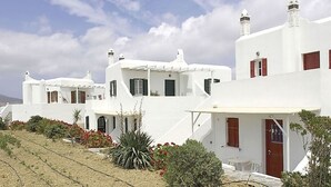 Una hilera de edificios blancos con techos planos y contraventanas rojas, rodeados de jardines ajardinados y un cielo despejado.