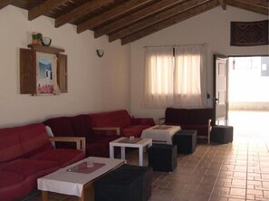 A living room with a red sofa, a small table, and a window with curtains. - Peters Kool Pool Studios (Kos)