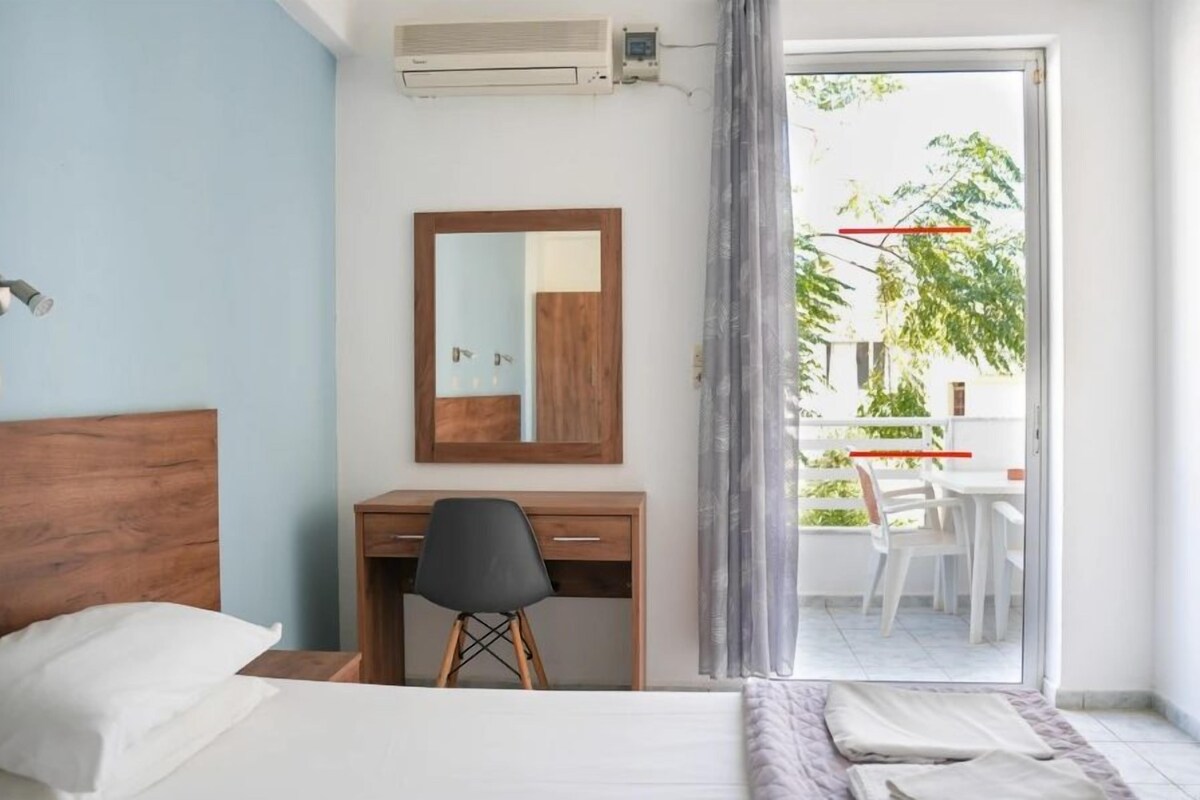 A hotel room with a bed, a desk, a chair, a mirror, and a balcony with a table and chairs.
