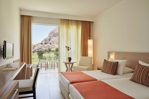 Habitación de hotel con cama, escritorio, silla y vistas a un paisaje montañoso.