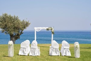 Preparación para una ceremonia de boda con un arco blanco y sillas, con vistas a un cuerpo de agua.