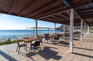 Un patio al aire libre con mesas y sillas, con vistas a una playa y el océano.