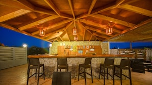 An outdoor bar area with stone walls, wooden ceiling beams, and wicker chairs. - Sea Harmony (Rhodes)
