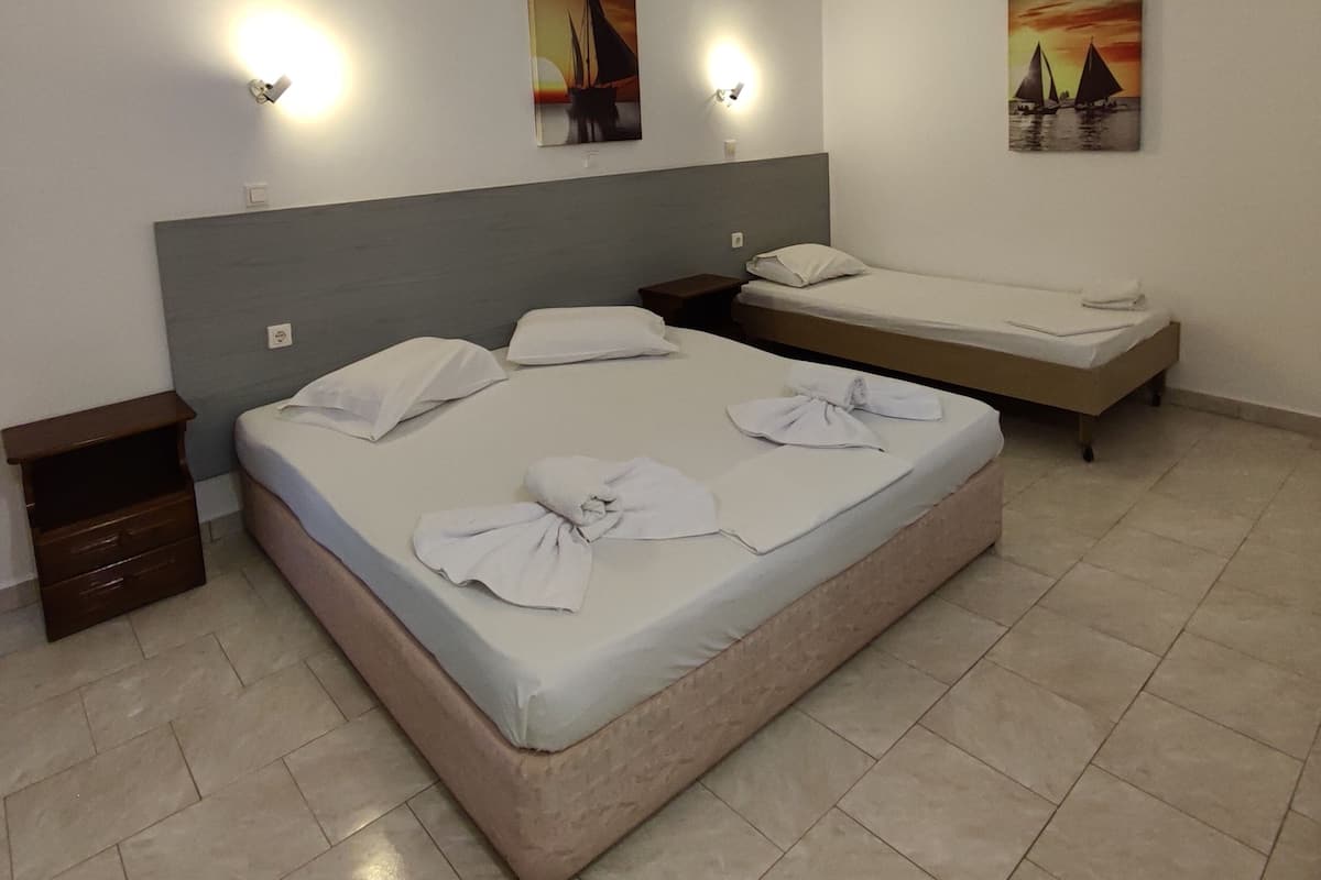 A hotel room with a large bed, two smaller beds, a nightstand, and artwork on the walls.