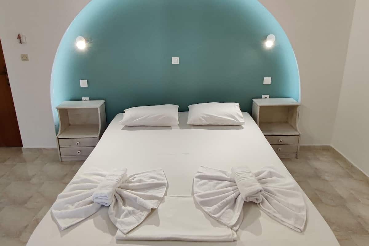 A bed with white linens and bows, two bedside tables, and a teal-colored headboard.