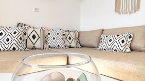 A living room with a sofa, patterned cushions, a glass fishbowl on a coffee table, a wall-mounted TV, and a macrame wall hanging. - Sea Harmony (Rhodes)
