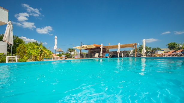 A clear blue pool with lounge chairs and umbrellas, surrounded by greenery and a clear sky. - Sea Harmony (Rhodes)