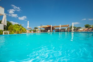 A clear blue pool with lounge chairs and umbrellas, surrounded by greenery and a clear sky. - Sea Harmony (Rhodes)