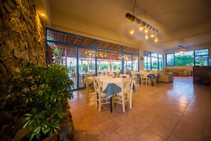 A spacious dining area with large windows, a stone wall, and hanging lights. - Sea Harmony (Rhodes)