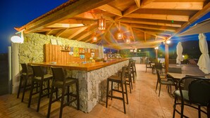An outdoor bar area with stone walls, wooden bar counter, and multiple seating options including bar stools and tables. - Sea Harmony (Rhodes)