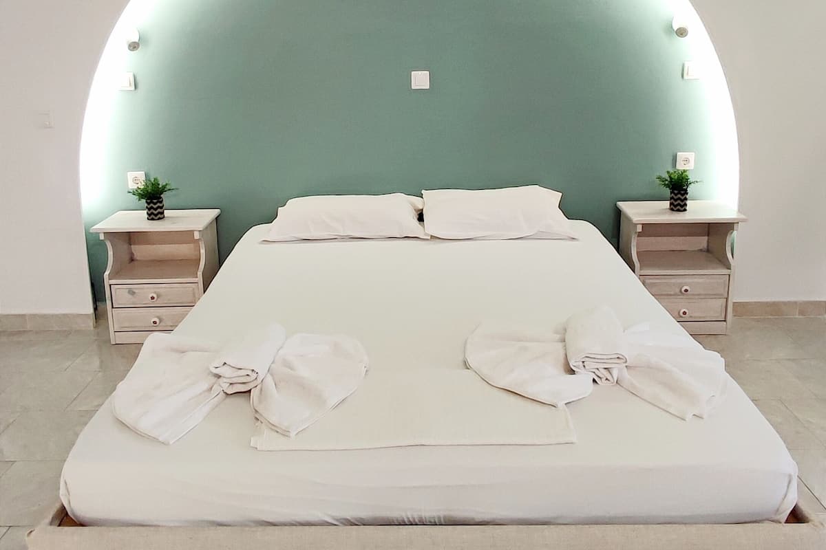 A modern bedroom with a curved ceiling, a large bed with white linens, two bedside tables with decorative plants, and a light green wall.