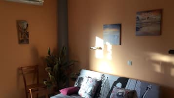 Una sala de estar con sofá, una silla, planta en maceta y decoración en la pared.