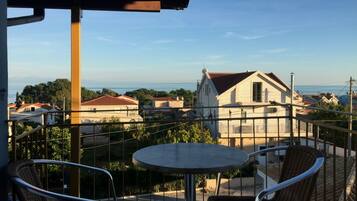 Un balcón con mesa y sillas, con vista a una zona residencial de casas y una vista despejada del mar.