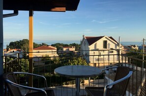 A balcony with a table and chairs, overlooking a residential area with houses and a clear view of the sea. - Eleni Studios (Kefalonia)