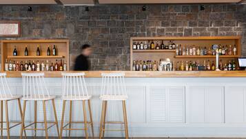 A bar area with wooden stools, shelves of liquor bottles, and a stone wall backdrop.