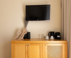A wooden cabinet with a television mounted above it, a feathered plant, a coffee maker, and a kettle.