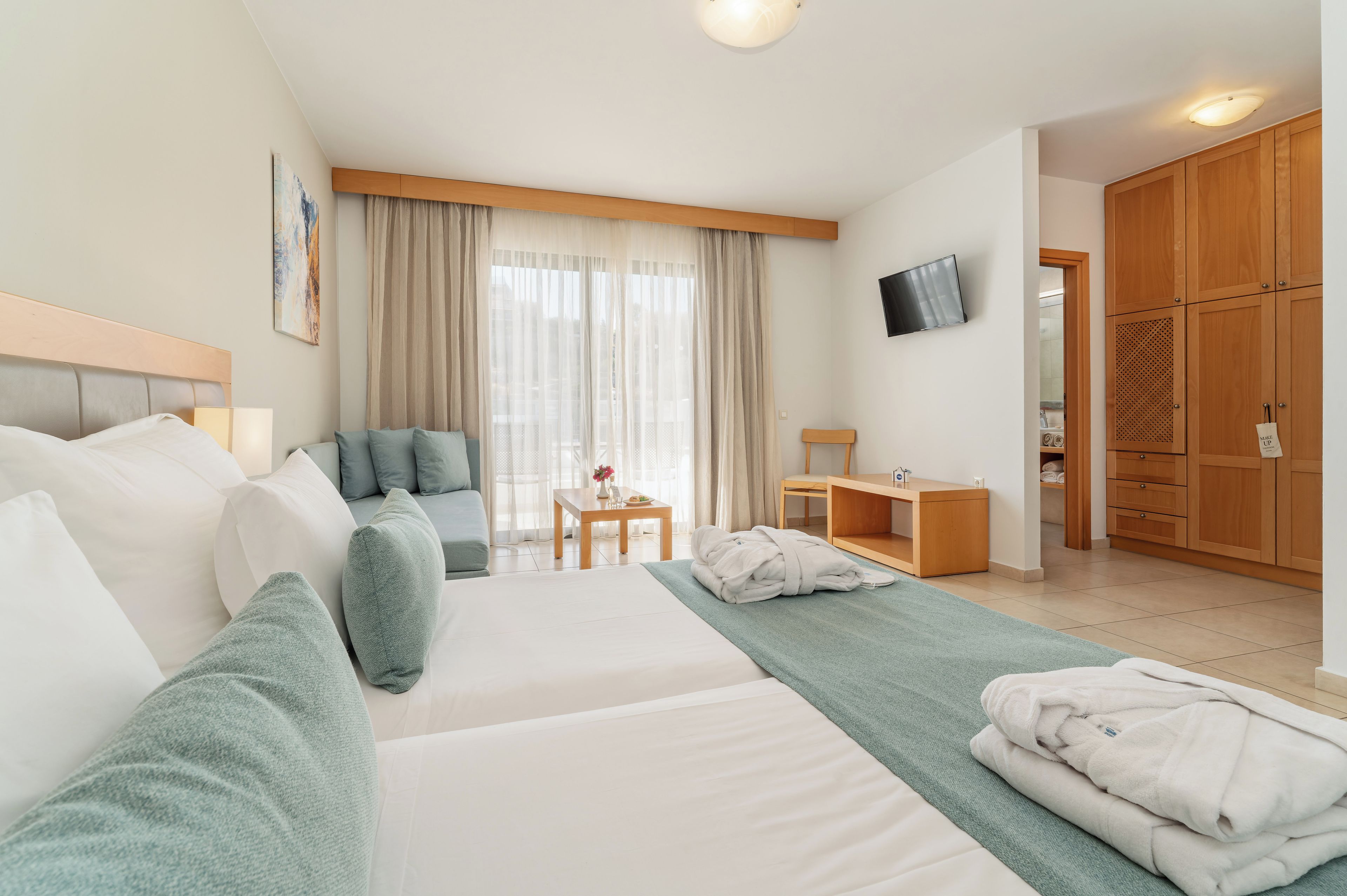 Una habitación de hotel con cama, sofá, una mesita, televisor y armario.