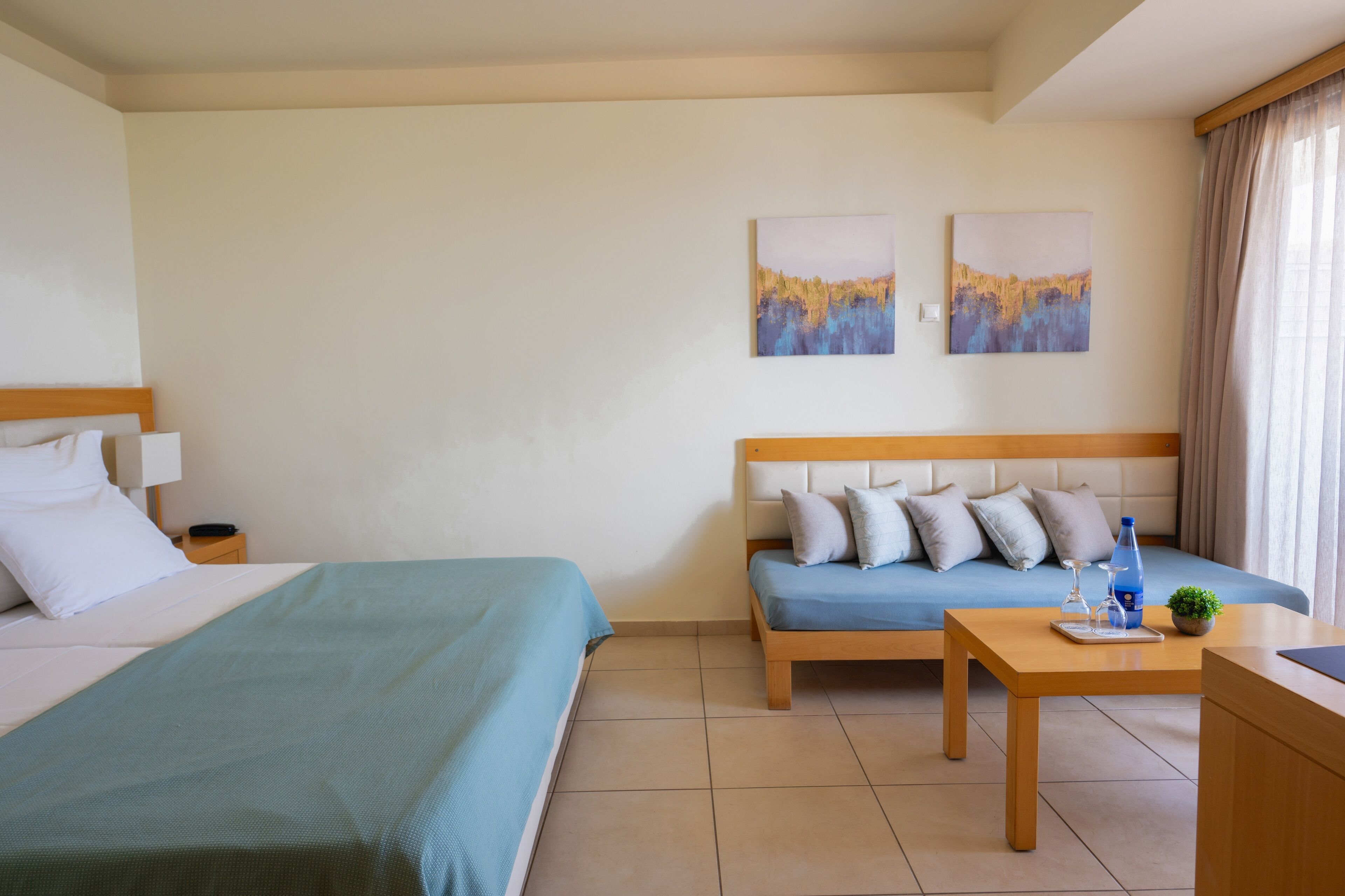 Ein Hotelzimmer mit einem Bett, einer Couch, einem kleinen Tisch mit Pflanze und zwei abstrakten Bildern an der Wand.