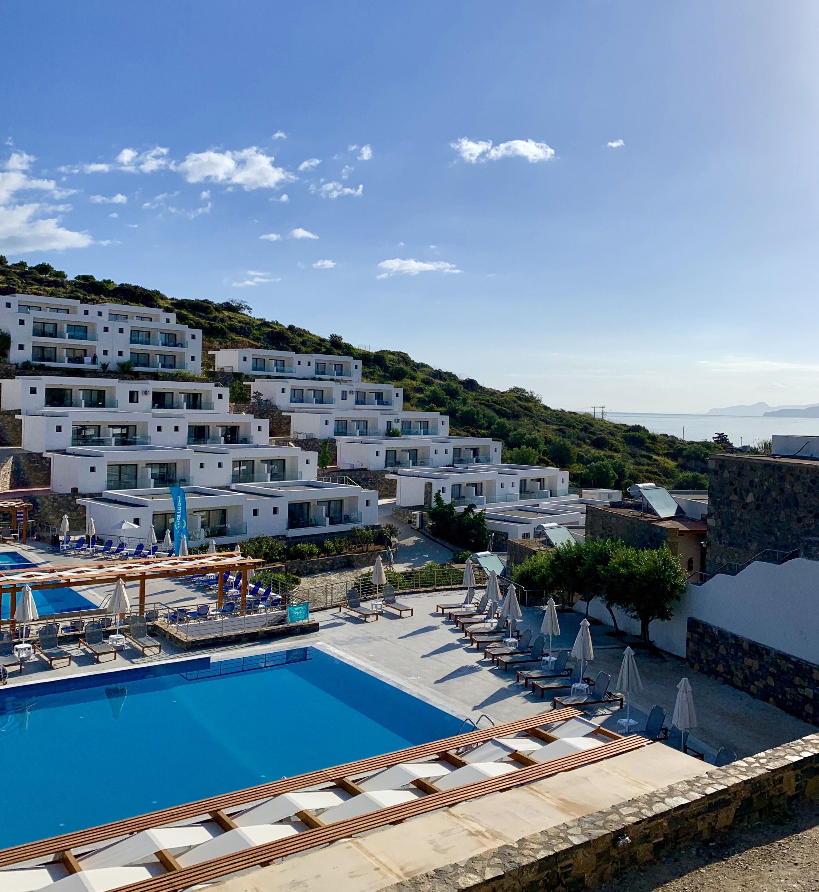 Un resort con piscina, lettini prendisole e moderni edifici bianchi con balconi.