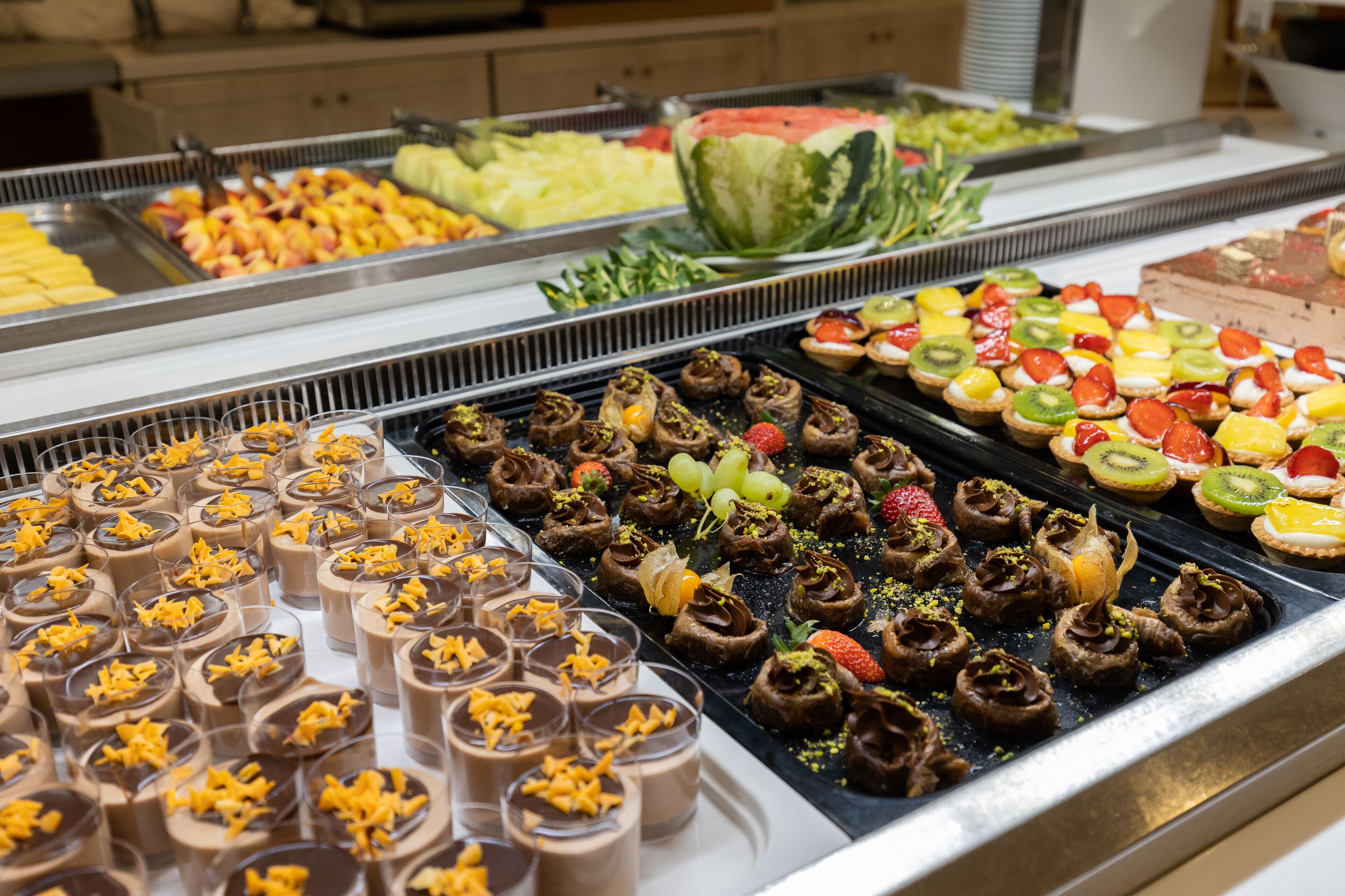 A buffet with various food options including fruits, desserts, and a watermelon centerpiece.